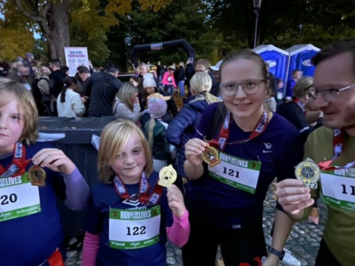 Personer visar upp medaljer efter ett lopp utomhus, iförda nummerlappar och löparkläder i en folkmassa.