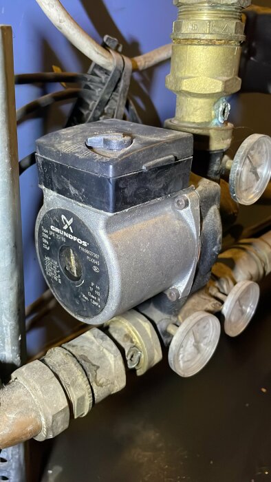 Cirkulationspump av märket Grundfos, monterad på rörsystem, med kablar och ventiler synliga.