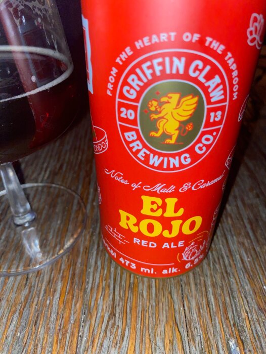 Röd burk med "Griffin Claw Brewing Co."-logga och texten "El Rojo Red Ale", bredvid ett glas med mörkröd dryck.
