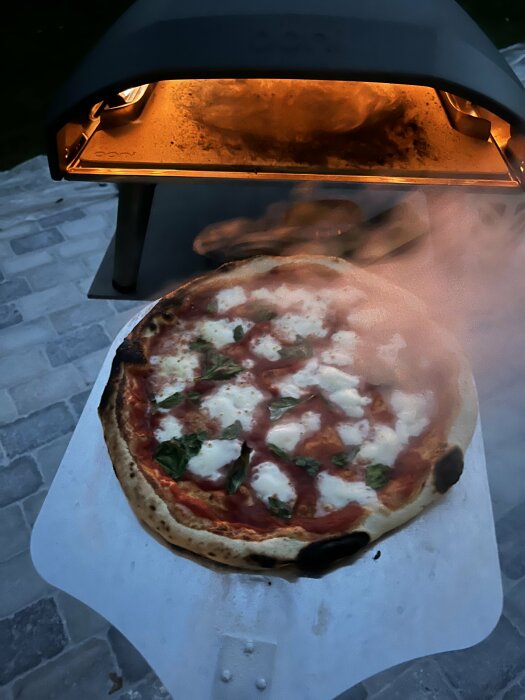 Pizza med brända kanter i en ugn utomhus.