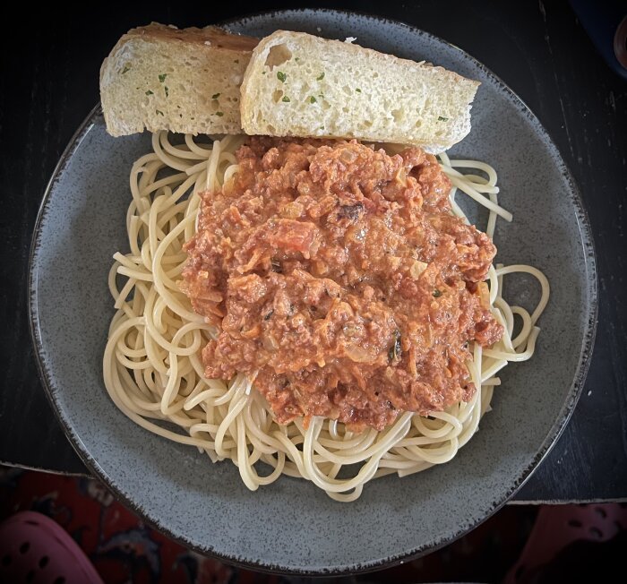 Spaghetti med köttfärssås gjord av chorizofärs, serverad med vitlöksbröd på tallrik.