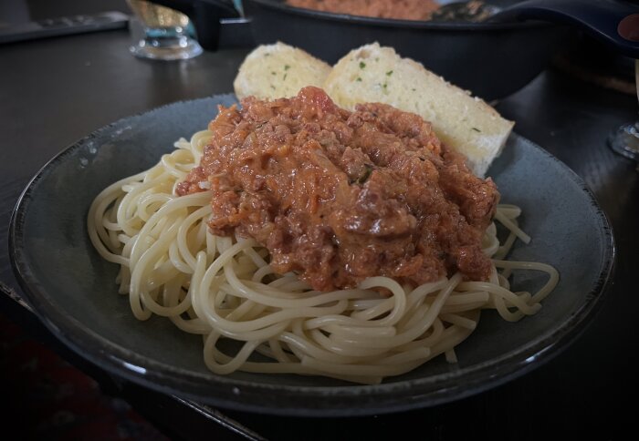 Spaghetti med köttfärssås gjord på choritzofärs, serverad med vitlöksbröd på en mörk tallrik.