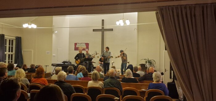 Band spelar på en scen under en gospelkonsert i en kyrksal, inför en publik av sittande åhörare.