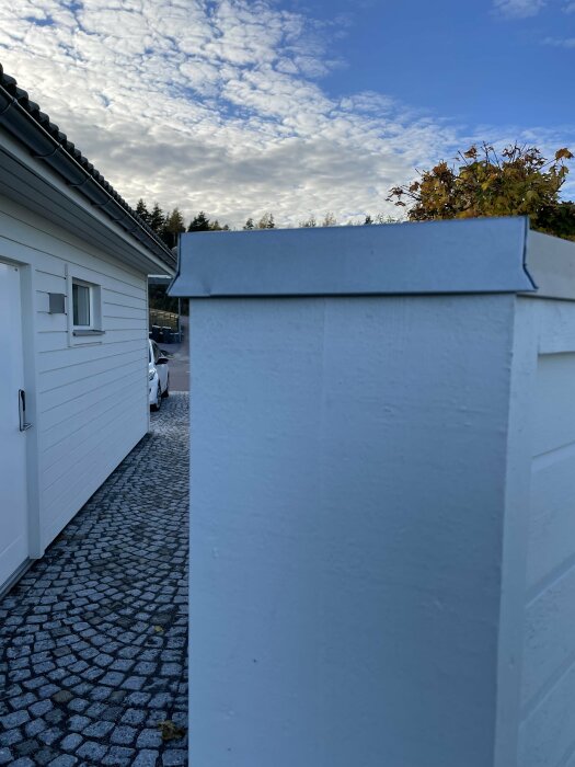 Bucklig plåt på en vit träpelare framför ett garage under en molnig himmel.