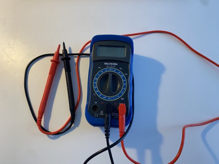 Digital multimeter med röda och svarta provsladdar på vit bakgrund.