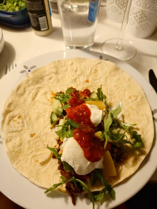 Tortilla fylld med grönsaker, creme fraiche och Djävulssås, serverad på en tallrik.