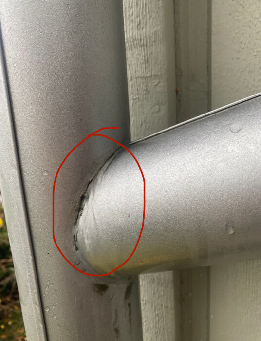 Läckande stuprörsskarv vid husvägg markerad med röd cirkel.
