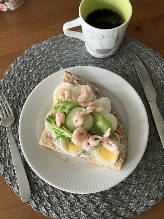 Räkmacka på hönökaka med skagenröra, ägg och räkor på en vit tallrik. En kopp kaffe står bredvid på bordet.