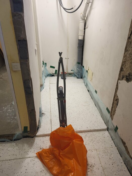 Golv med cellplast och golvbrunn i ett blivande duschrum, rörinstallation syns. Orange skyddsmaterial på golvet.