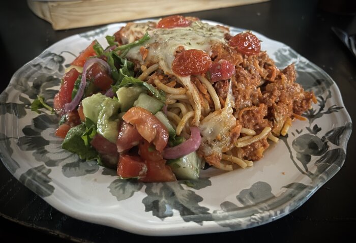 Pastagratäng med choritzofärs, ost och tomater, serverad med sallad innehållande picklad rödlök, vattenmelon och avokado på en blommig tallrik.