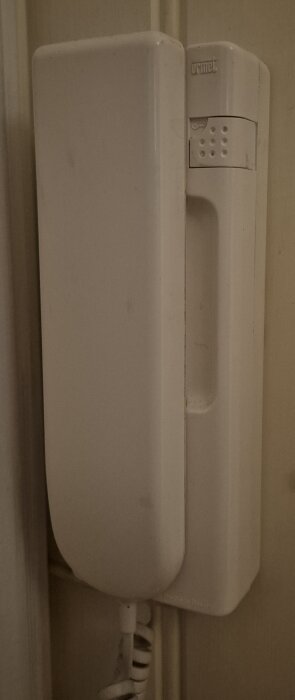 Vit gammal porttelefon av märket Urmet monterad på en vägg.