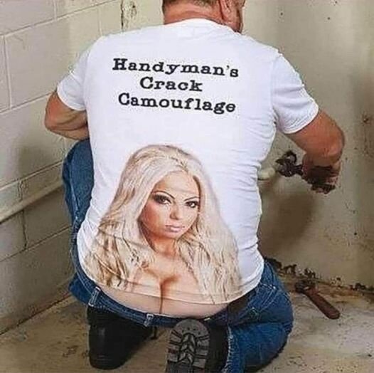 Person i vit t-shirt med text "Handyman's Crack Camouflage" och tryck av en kvinna på ryggen arbetar med rör i ett hörn av ett rum.