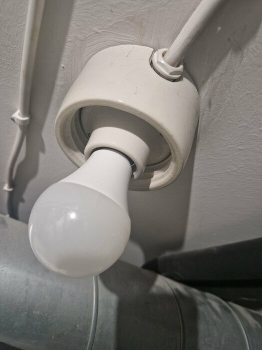 Vinklad ljusarmatur med glödlampa installerad i taket nära ventilationsrör.