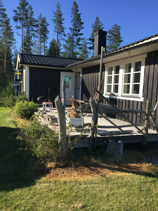 Fritidshus i trä med en veranda, omgiven av gräs och tallar, under en klarblå himmel i Sör Imnäs, Ramsele.