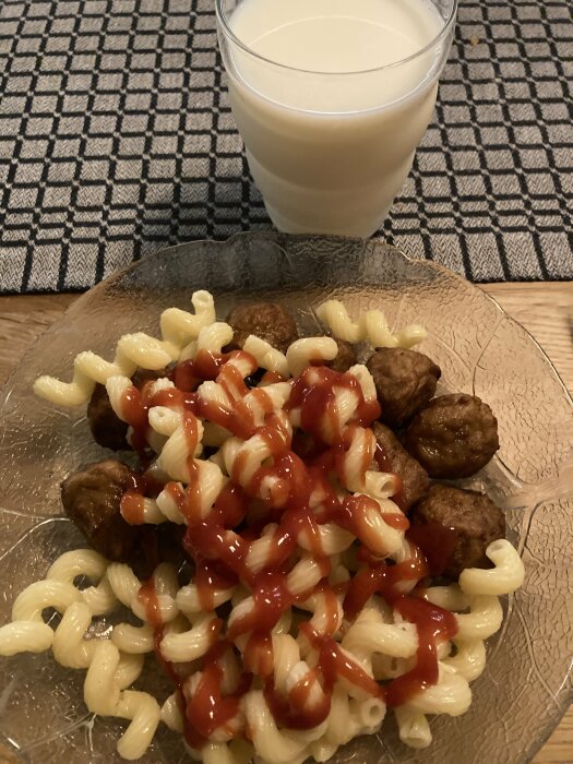 Pasta och köttbullar med ketchup på ett glasfat, serverat med ett glas mjölk.