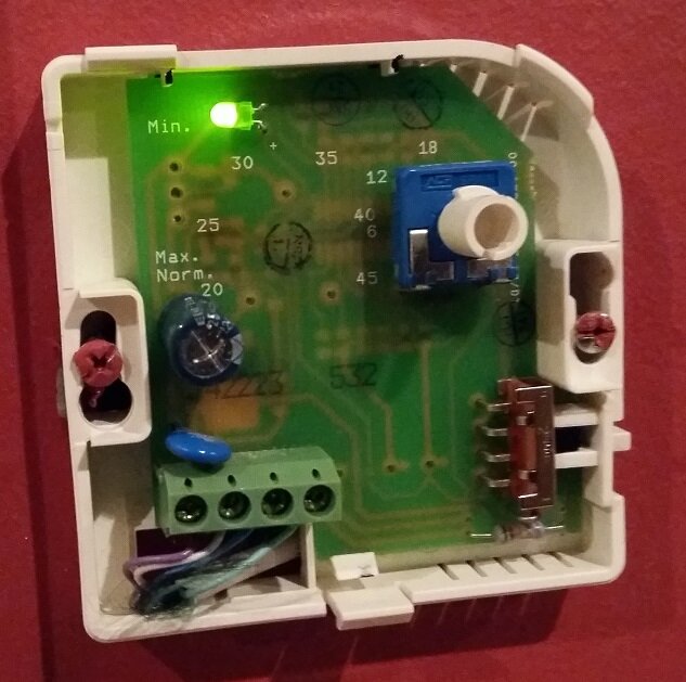 Termostat för vattenburen golvvärme i vit plastkapsling med grön kretskort och komponenter, inklusive lysdiod och vridpotentiometer.