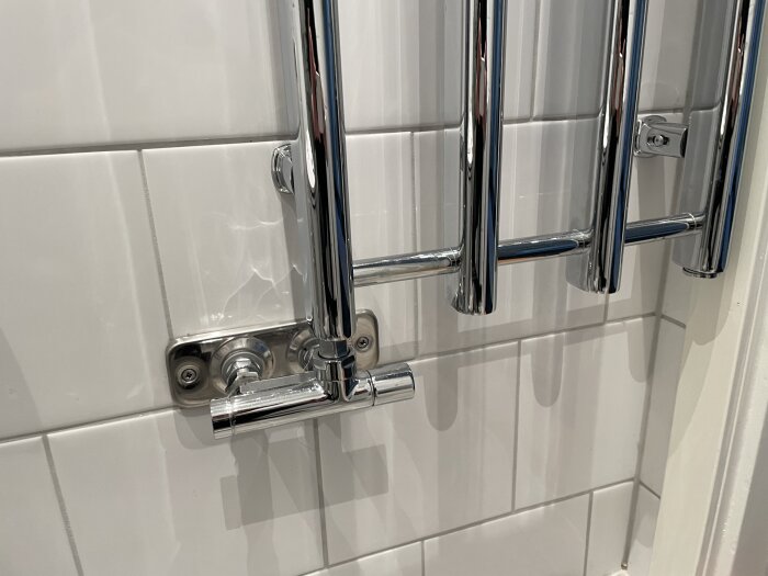 Kromad handdukstork installerad nära dörrfoder, med synliga rör och väggfästen på kakelvägg.