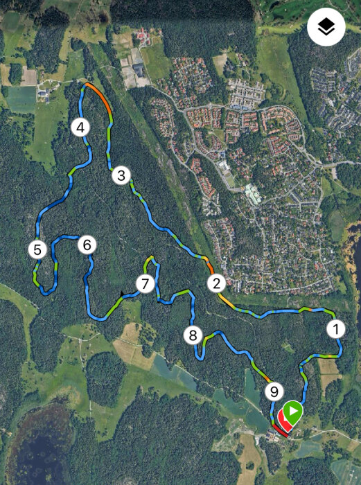 Satellitbild med en markerad trailbana i en skogs- och stadsområde, numrerade checkpoints och ett startområde med grön pil i nederkant av bilden.