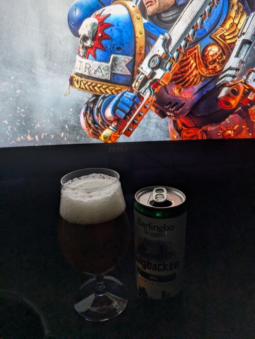 Ett glas öl och en ölburk med texten "Galgbacken IPA" från Barlingbo framför en datorskärm med ett spelmotiv.