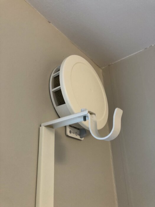 Ventilationslucka på väggen i ett rum, med en rund skyddsskiva och en konsol under.