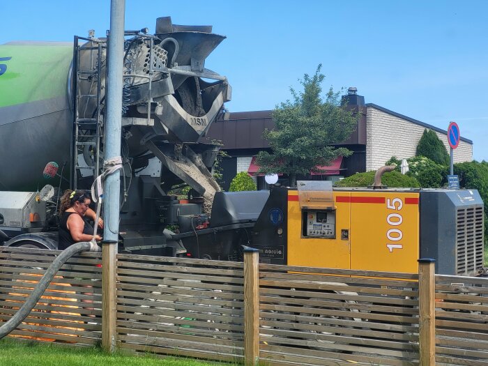 Betongbil och pumpstation användes vid gjutning. En person övervakar processen. Slang kopplad från betongbilen till pumpen, solig dag.