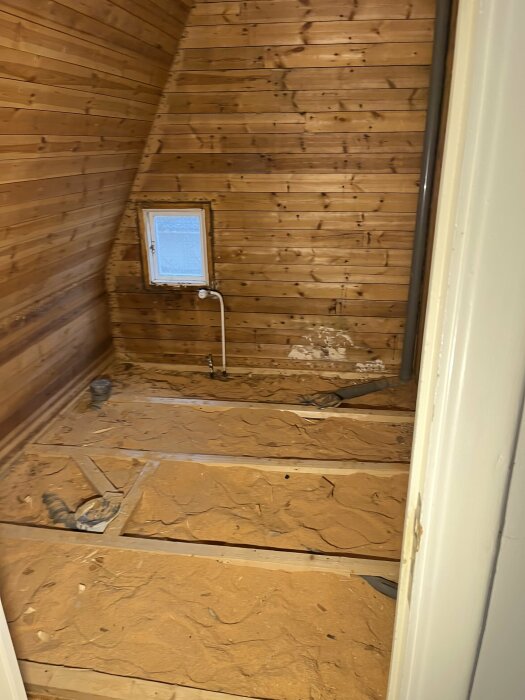 Renoveringsprojekt med träväggar och exponerade bjälkar i ett litet badrum, förberett för gips eller plywood före tätskikt och kakelsättning.