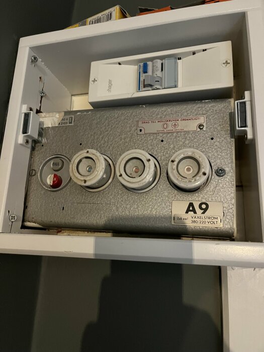 Elcentral med 20A säkring och porslinssäkringar i ett skåp med märkningen "A9 Våxelström 380/220 Volt".