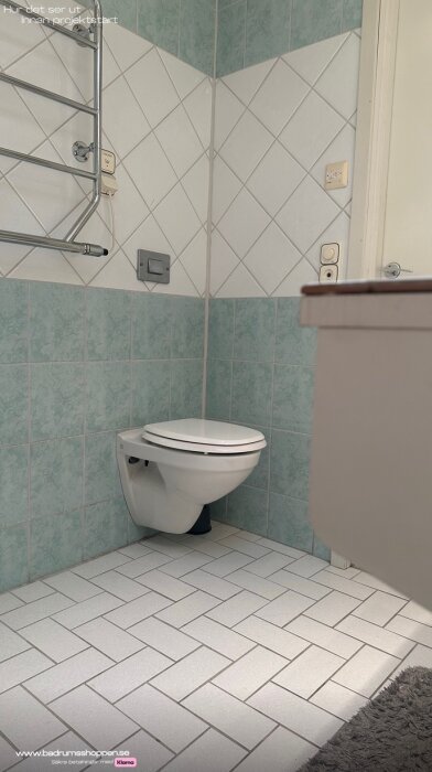 Nuvarande badrum med ljusblå och vita kakelväggar, vägghängd toalett och ljust klinkergolv inför kommande renovering.