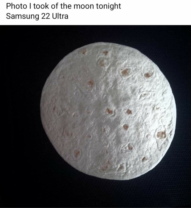 Rund tortilla med mörka fläckar på svart bakgrund.