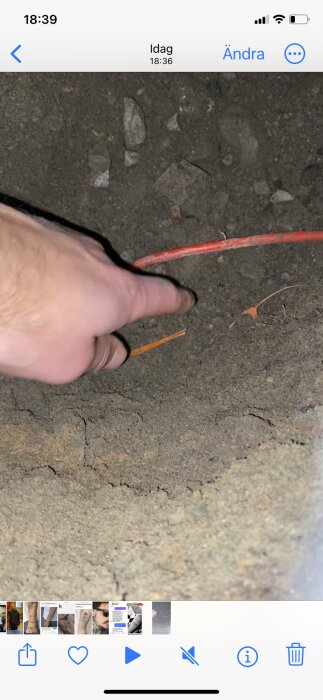 Hand pekar på orange kabel i jord.