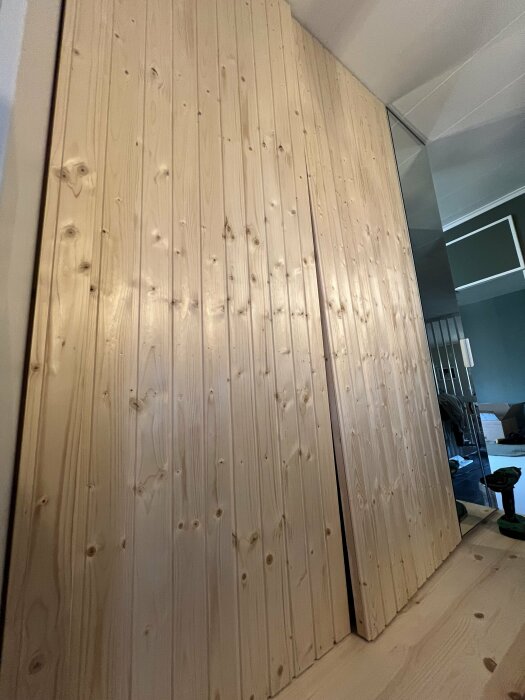 Garderobsdörrar av bastupanel, där en dörr glipar nertill och den andra upptill, med borrmaskin på golvet bredvid.