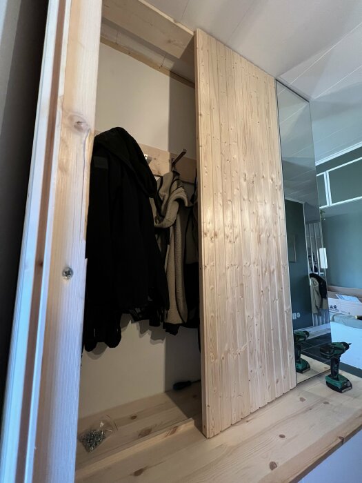 Garderobsdörrar av bastupanel, en glipar och är skev. Verktyg syns bredvid.
