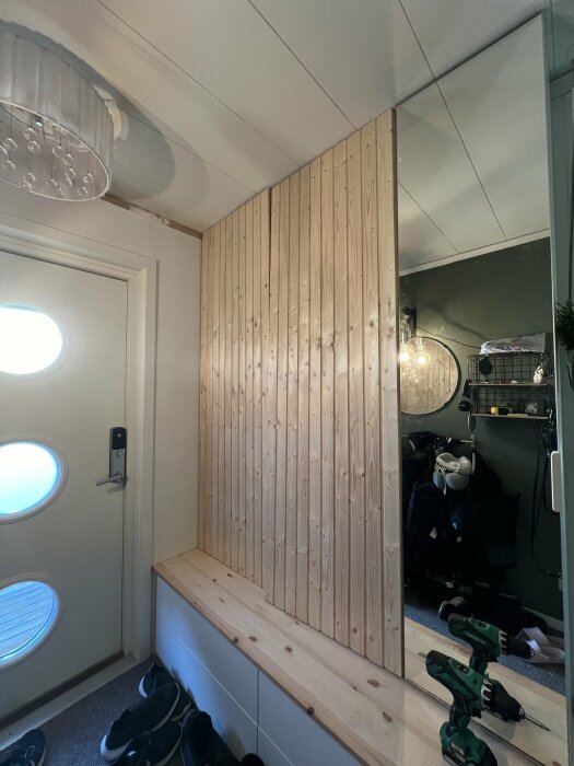 Garderobsdörrar av bastupanel där högra dörren är feljusterad nertill och vänstra upptill, verktyg synliga i hall med spegel och stängd dörr.