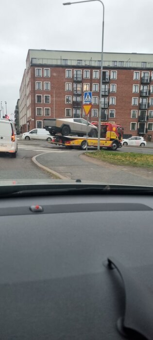 Bil transporteras på bärgningsbil vid korsning i Stockholm, byggnad i bakgrunden.