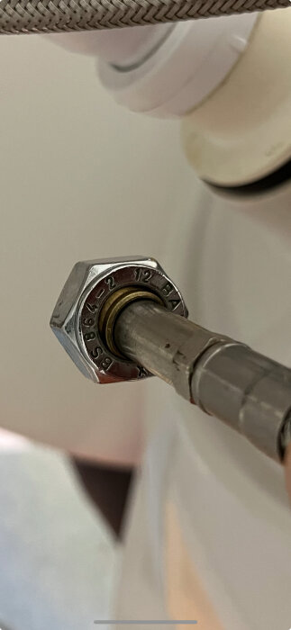 Något metallrör med en gängad koppling och ingraverad text, potentiellt en anslutningsslang för blandare eller ballofix.