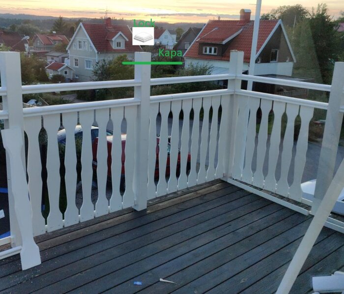 Vit träbalkong med dekorativa balustrader och en stående pelare som ska kapas. Bakgrund med hus och solnedgång.