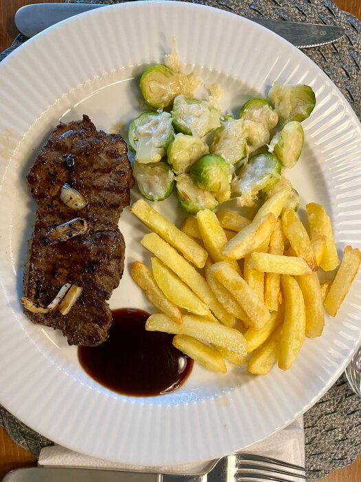 Tallrik med ryggbiff, pommes frites och brysselkål täckt med parmesan, serverad med en klick rödvinssås.