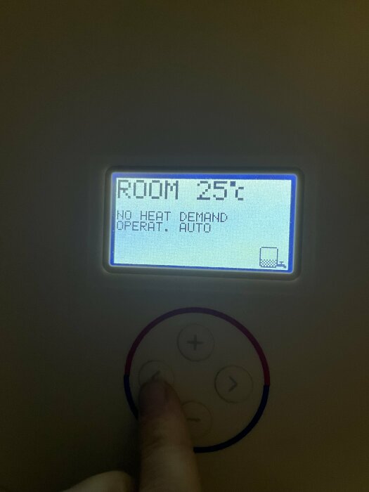 Termostatdisplay visar "ROOM 25°C", "NO HEAT DEMAND", och knappar med finger som trycker på en menyknapp.