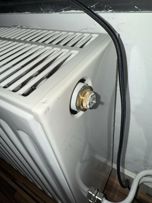 Radiator med borttagen termostat, exponerade gängor och ledning synliga mot en vägg. Problem med att fästa ny termostatadapter.