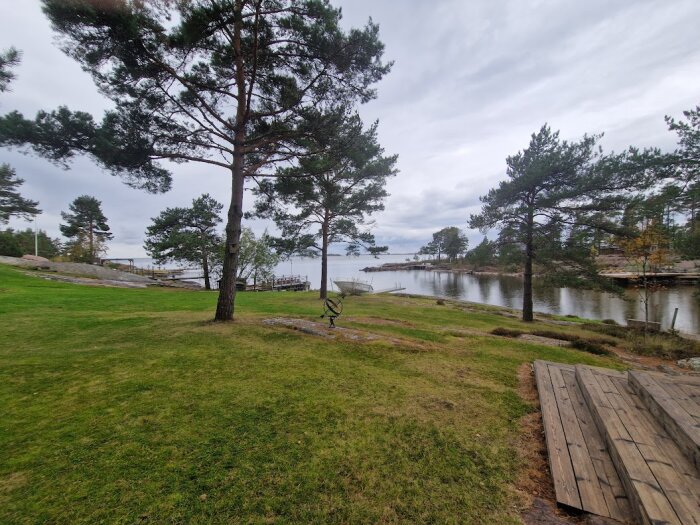 Utsikt över träd, gräs och ett vattendrag med bryggor och en mulen himmel.