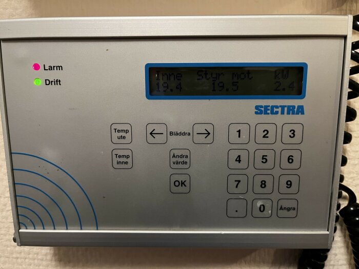Närbild på en manövreringspanel av märket SECTRA med text och knappar, där en larm- och driftdiod lyser. Visar temperatur och elförbrukning.
