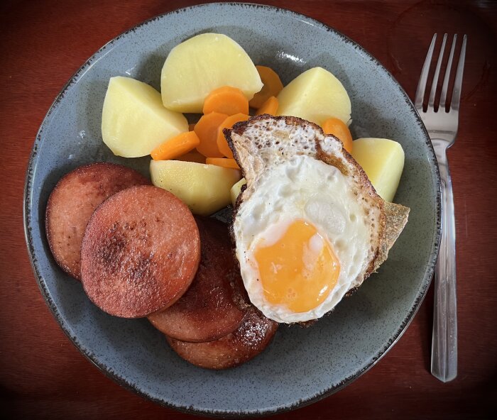 Tallrik med falukorv, kokt potatis, kokta morötter och ett stekt ägg.