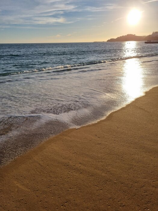 Solnedgång över en portugisisk strand med vågor som sköljer in över den gyllene sanden.