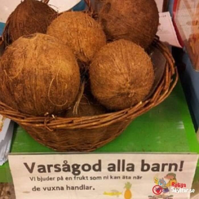 Kokosnötter i en korg med en skylt som uppmanar barn att ta en frukt medan de vuxna handlar.