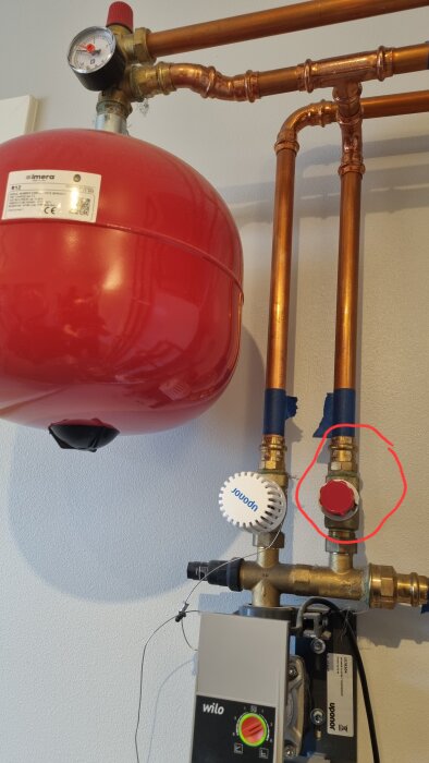 Röd expansionskärl och kopparrör i ett värmesystem med tryckmätare och rörkopplingar.