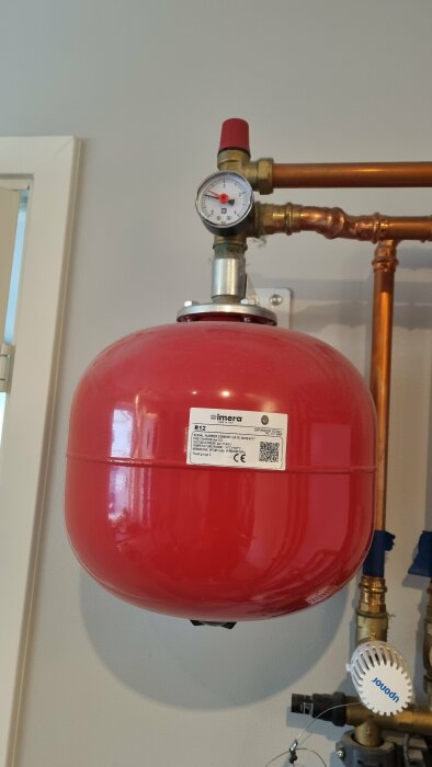 Röd expansionskärl med manometer installerad på kopparrör.