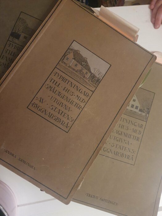 Två böcker med illustrationer av typritningar för hus och smålägenheter från Statens Byggnadsbyrå, speglar gammal arkitektur.