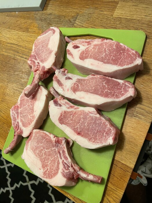 Sex stycken Iberico-kotletter på en grön skärbräda, redo för tillagning enligt recept.