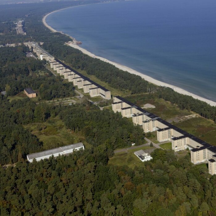 Flygfoto av långa byggnader längs en strandlinje omgivna av skog, påminner om arkitekturen i Prora-komplexet.