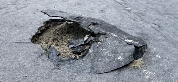 Närbild av en takpanna med avflagat ytskikt, avslöjar underliggande sandblandning och skador i materialet.